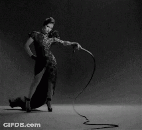 A Woman In A Dress Is Holding A Whip In Her Hand . GIF