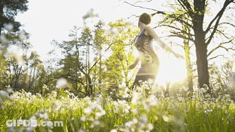 A Woman In A Dress Is Standing In A Field Of White Flowers GIF