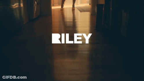 A Woman In A Dress Is Standing In A Hallway With The Word Riley On The Bottom GIF