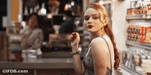 A Woman In A Dress Is Standing In Front Of A Counter In A Store Eating A Candy Bar . GIF