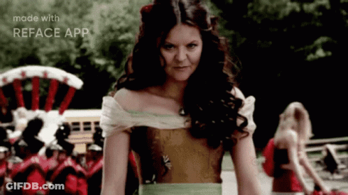 A Woman In A Dress Is Standing In Front Of A Crowd And The Words Made With Reface App Are On The Bottom Of The Screen GIF