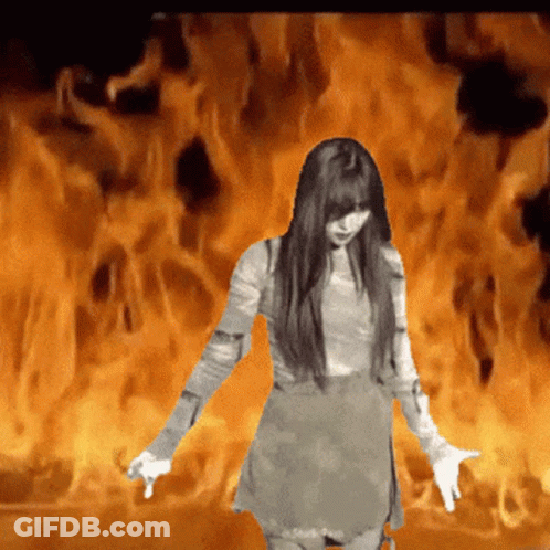 A Woman In A Dress Is Standing In Front Of A Fire GIF