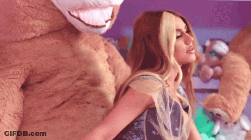 A Woman In A Dress Is Standing Next To A Stuffed Animal GIF