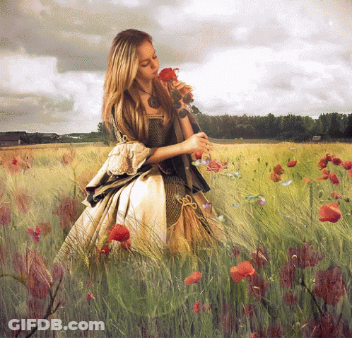 A Woman In A Dress Smells A Rose In A Field GIF