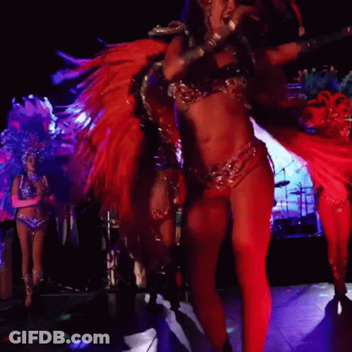 A Woman In A Feathered Costume Is Dancing In A Dark Room GIF