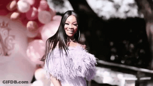 A Woman In A Feathered Dress Is Standing In Front Of Balloons And Smiling . GIF
