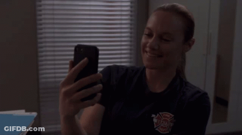 A Woman In A Firefighter Uniform Is Taking A Selfie With Her Cell Phone GIF