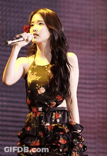 A Woman In A Floral Dress Holds A Microphone In Her Hand GIF