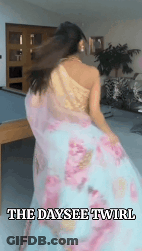 A Woman In A Floral Dress Is Dancing In A Room With The Words The Daysee Twirl Above Her GIF