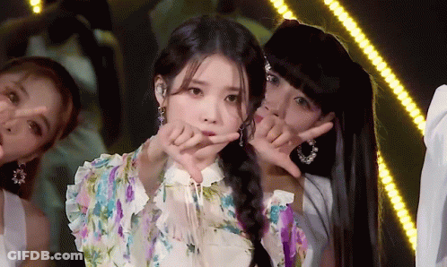 A Woman In A Floral Dress Is Making A Heart Shape With Her Fingers GIF