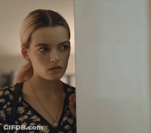 A Woman In A Floral Dress Is Peeking Behind A Door GIF