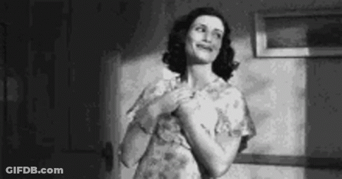 A Woman In A Floral Dress Is Standing In A Room And Smiling . GIF