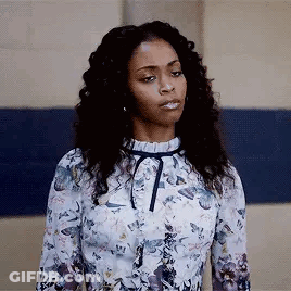 A Woman In A Floral Dress Is Standing In Front Of A Blue Wall And Making A Funny Face . GIF