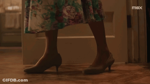 A Woman In A Floral Dress Is Standing In Front Of A Door With The Word Max On The Bottom Right GIF