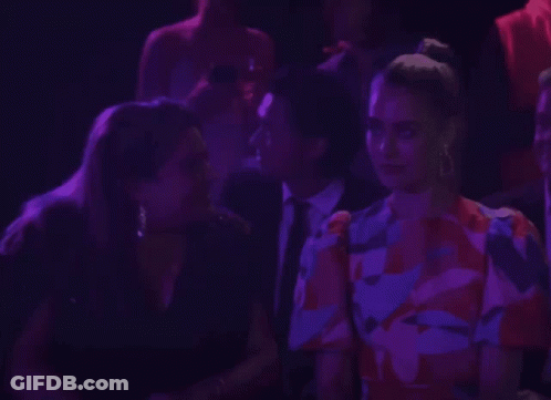 A Woman In A Floral Dress Talks To A Man In A Suit GIF