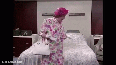 A Woman In A Floral Robe And Pink Hat Is Standing In Front Of A Bed In A Hospital Room . GIF