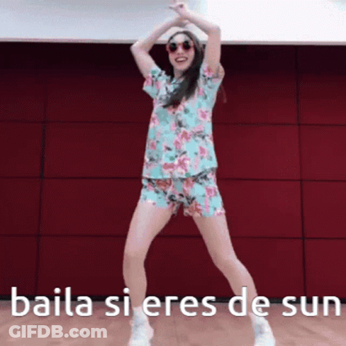 A Woman In A Floral Shirt And Shorts Is Dancing With The Words Baila Si Eres De Sun Above Her GIF
