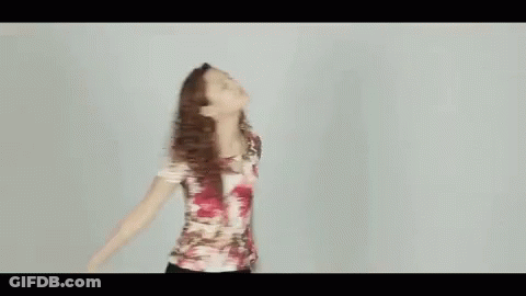 A Woman In A Floral Shirt Is Dancing With Her Arms Outstretched . GIF