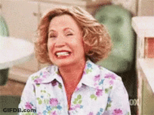 A Woman In A Floral Shirt Is Laughing While Sitting Down . GIF