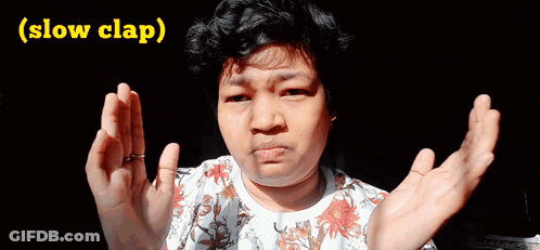A Woman In A Floral Shirt Is Making A Funny Face With Her Hands Outstretched And The Words Slow Clap Below Her GIF