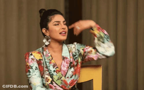 A Woman In A Floral Shirt Is Sitting In A Chair And Pointing At Her Face GIF