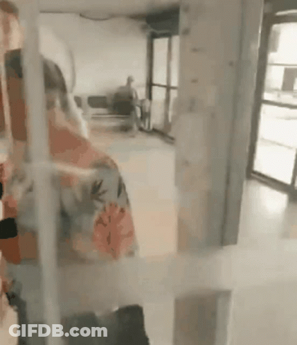 A Woman In A Floral Shirt Is Standing In A Room With A Glass Door . GIF
