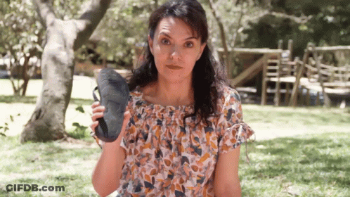 A Woman In A Floral Top Is Holding A Pair Of Shoes GIF