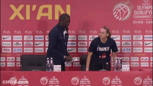 A Woman In A France Shirt Stands In Front Of A Xian Sign GIF