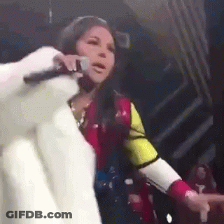 A Woman In A Fur Coat Is Singing Into A Microphone GIF