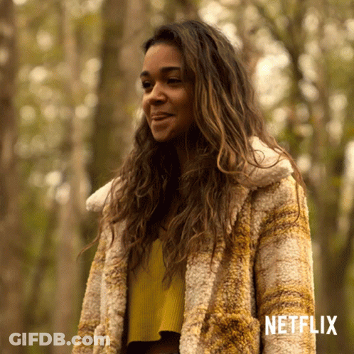 A Woman In A Fur Coat Is Standing In A Forest With Netflix Written On The Bottom GIF