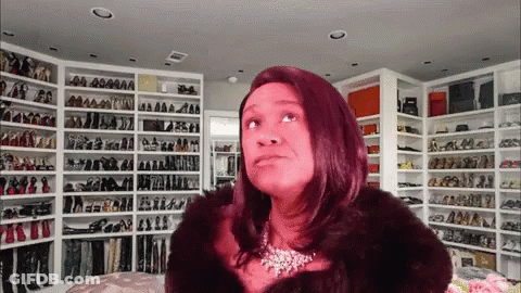A Woman In A Fur Coat Is Standing In Front Of A Wall Of Shoes GIF