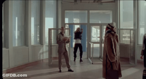 A Woman In A Fur Coat Stands In Front Of A Door That Says Tm GIF