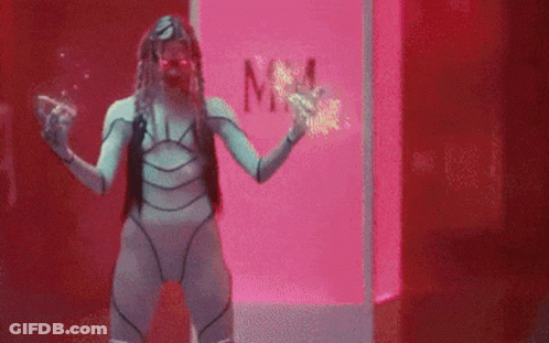 A Woman In A Futuristic Costume Is Standing In Front Of A Pink Box With The Word Mm On It . GIF