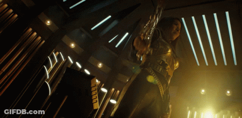 A Woman In A Futuristic Outfit Is Holding A Sword In A Dark Room GIF
