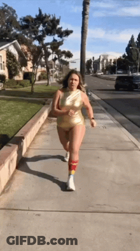 A Woman In A Gold Bodysuit Is Running On A Sidewalk GIF