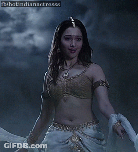 A Woman In A Gold Bra And White Pants Is Dancing In The Dark . GIF