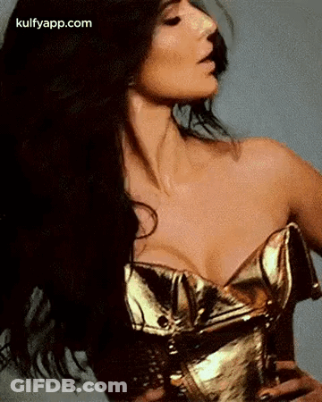 A Woman In A Gold Corset With Her Hair Blowing In The Wind Is Looking At The Camera . GIF