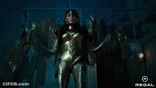 A Woman In A Gold Costume Is Standing In A Dark Room With A Regal Logo In The Corner GIF