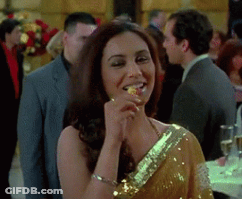 A Woman In A Gold Sequined Dress Is Eating A Piece Of Food GIF