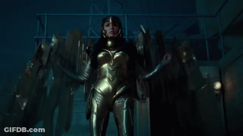 A Woman In A Gold Suit And Helmet Is Standing In A Dark Room GIF