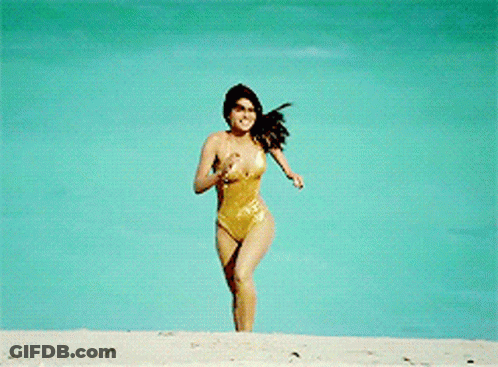 A Woman In A Gold Swimsuit Is Running On A Beach GIF