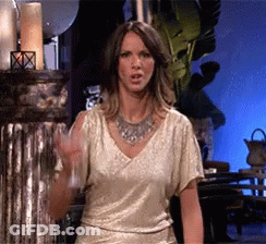 A Woman In A Gold Top And Silver Necklace Holds A Glass GIF