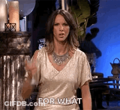 A Woman In A Gold Top Is Standing In Front Of A Metal Pillar And Says `` For What '' . GIF