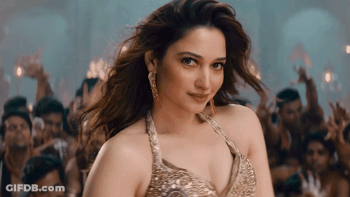 A Woman In A Gold Top Stands In Front Of A Crowd Of People GIF