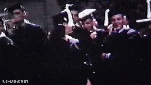 A Woman In A Graduation Cap And Gown Is Smiling In Front Of A Crowd Of People . GIF