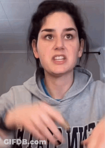 A Woman In A Gray Hoodie Is Making A Funny Face While Holding Her Hands Out . GIF