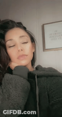 A Woman In A Gray Hoodie Is Sleeping With Her Eyes Closed And Her Hand On Her Face . GIF