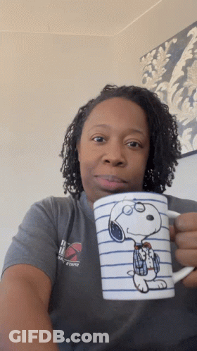 A Woman In A Gray Shirt Holds A Snoopy Coffee Mug GIF