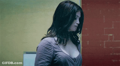 A Woman In A Gray Shirt Is Standing In Front Of A Red Wall . GIF