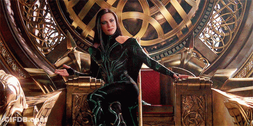 A Woman In A Green And Black Costume Is Sitting On A Gold Throne GIF